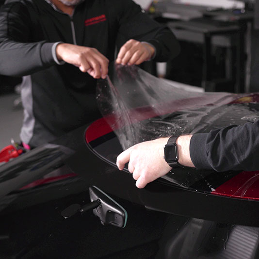 Installers position clear paint protection film on a car in a LLumar training photograph.