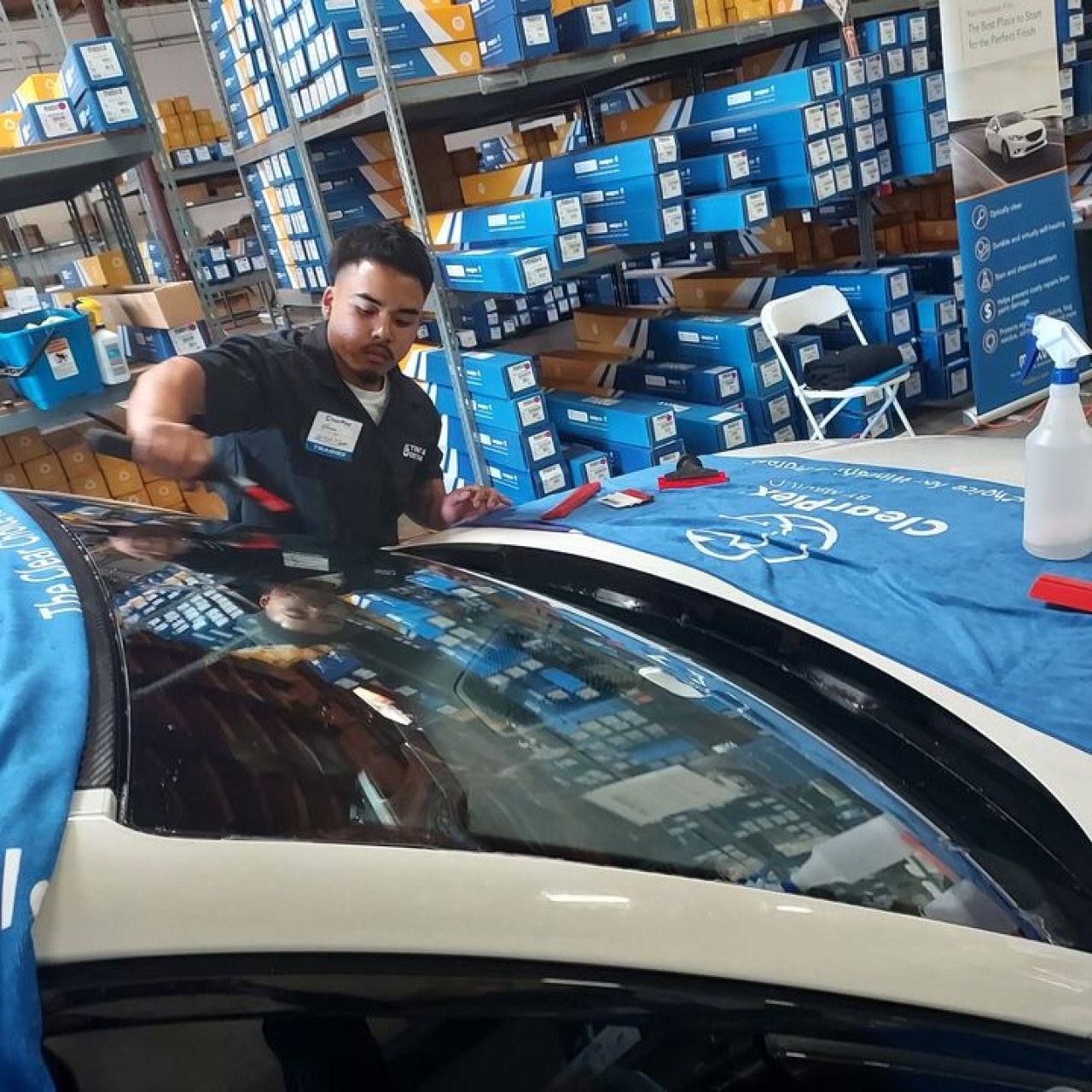 An installer works on a windshield beside a ClearPlex-branded protective cover.