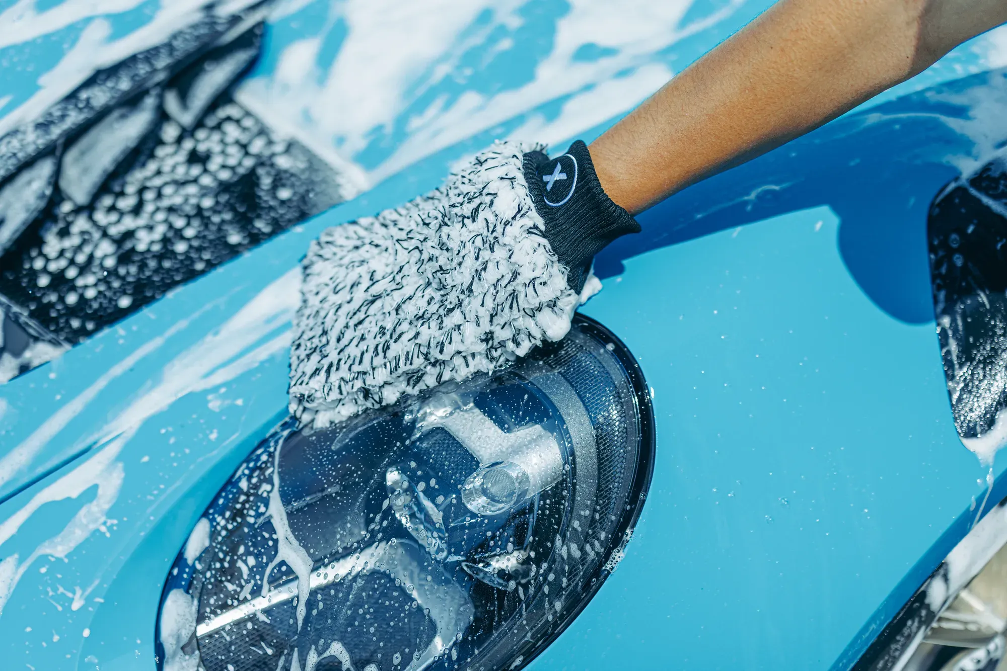 Wash mitt cleaning the foamy front bodywork of a blue car